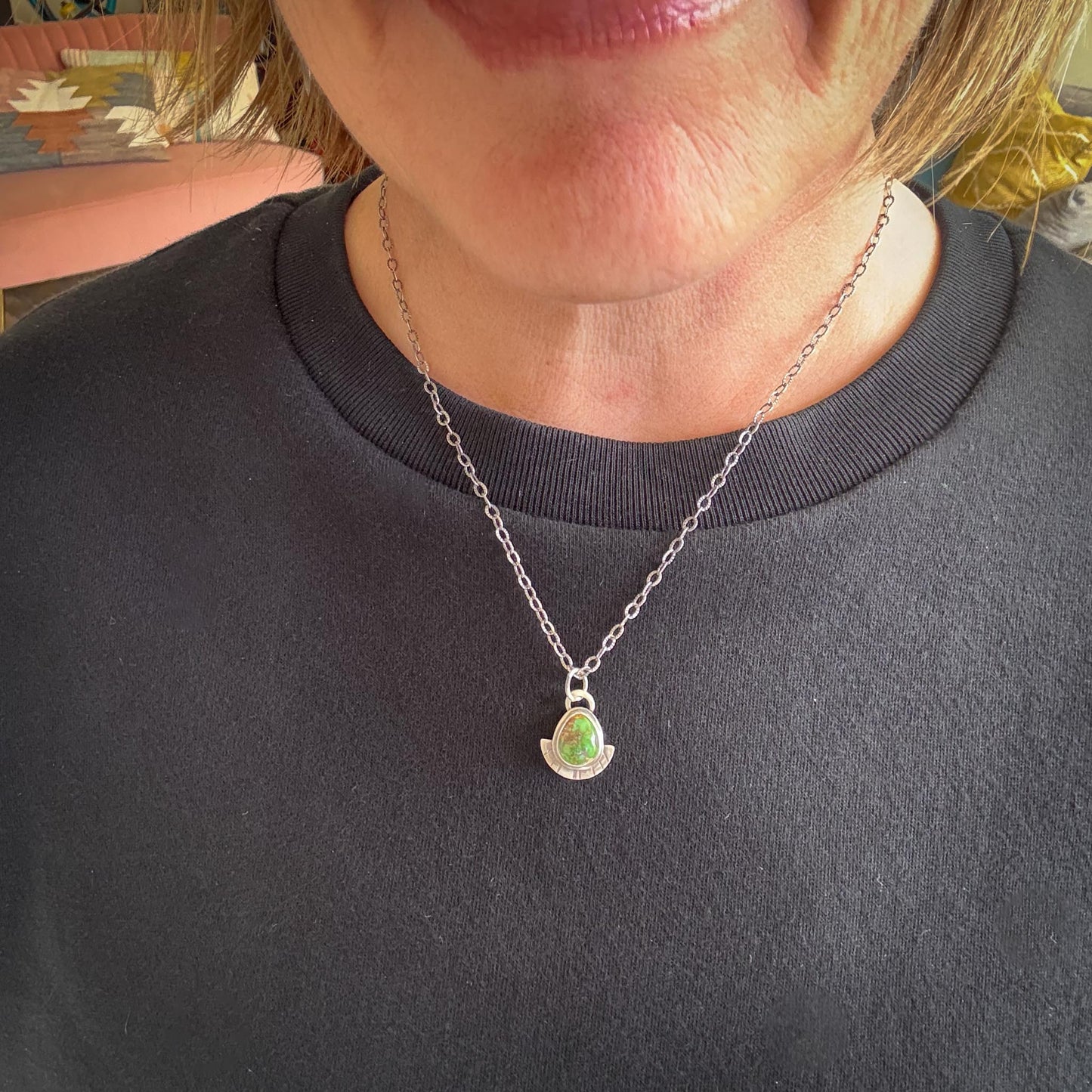 Necklace with a green pendant worn by a person in a gray shirt.