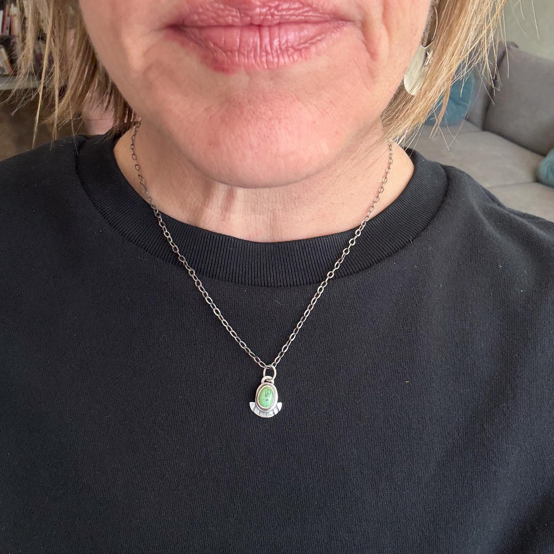 Person wearing a black sweater with a necklace featuring a green pendant.