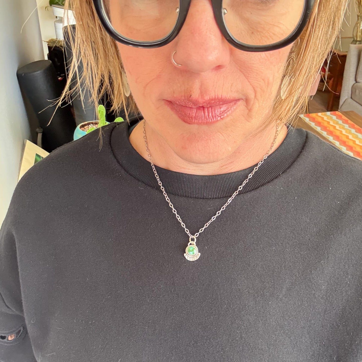 Person wearing a dark gray sweatshirt with a necklace featuring a green pendant.
