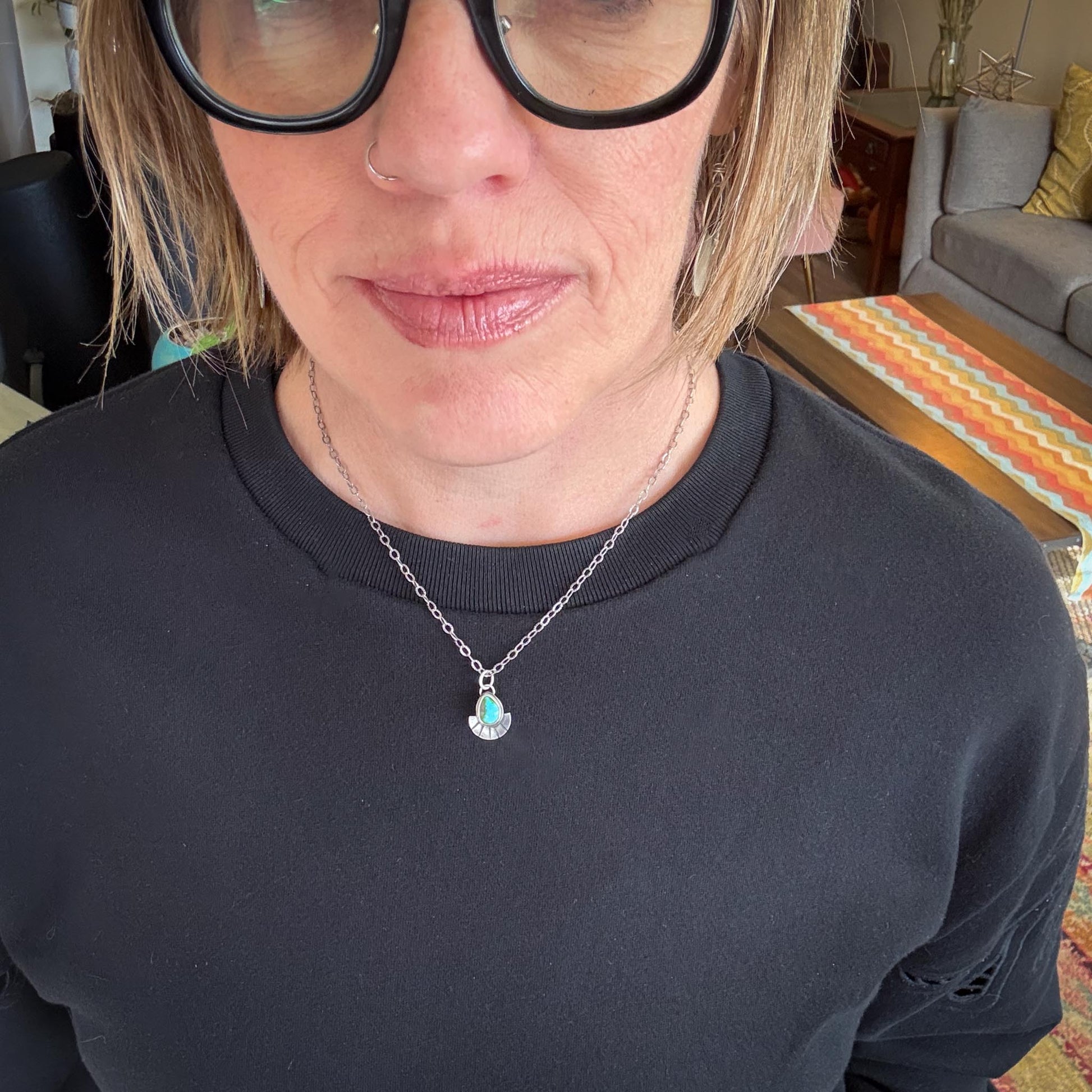 Person wearing a dark blue sweater with a necklace featuring a heart pendant.