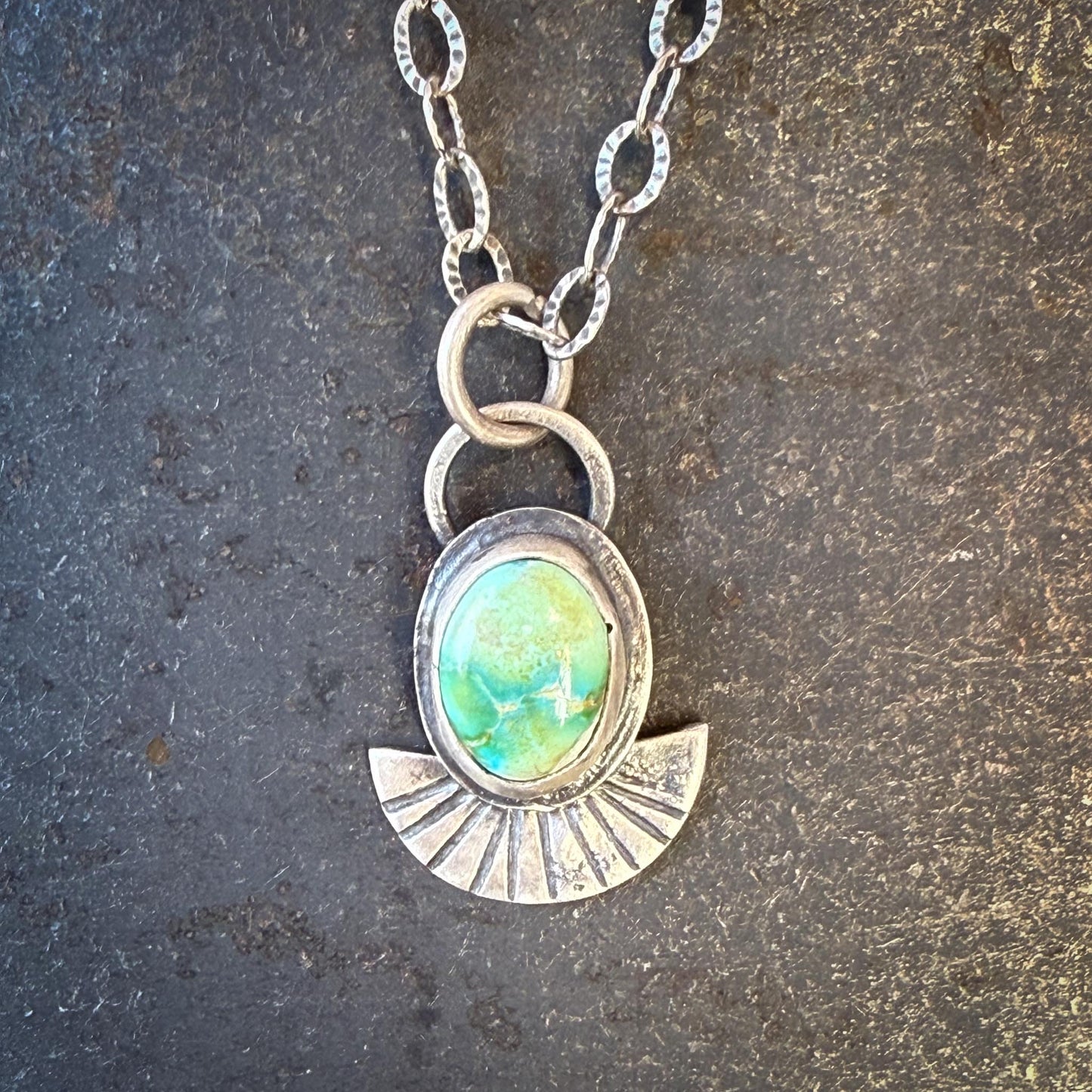 Necklace with a pendant featuring a green gemstone on a textured surface
