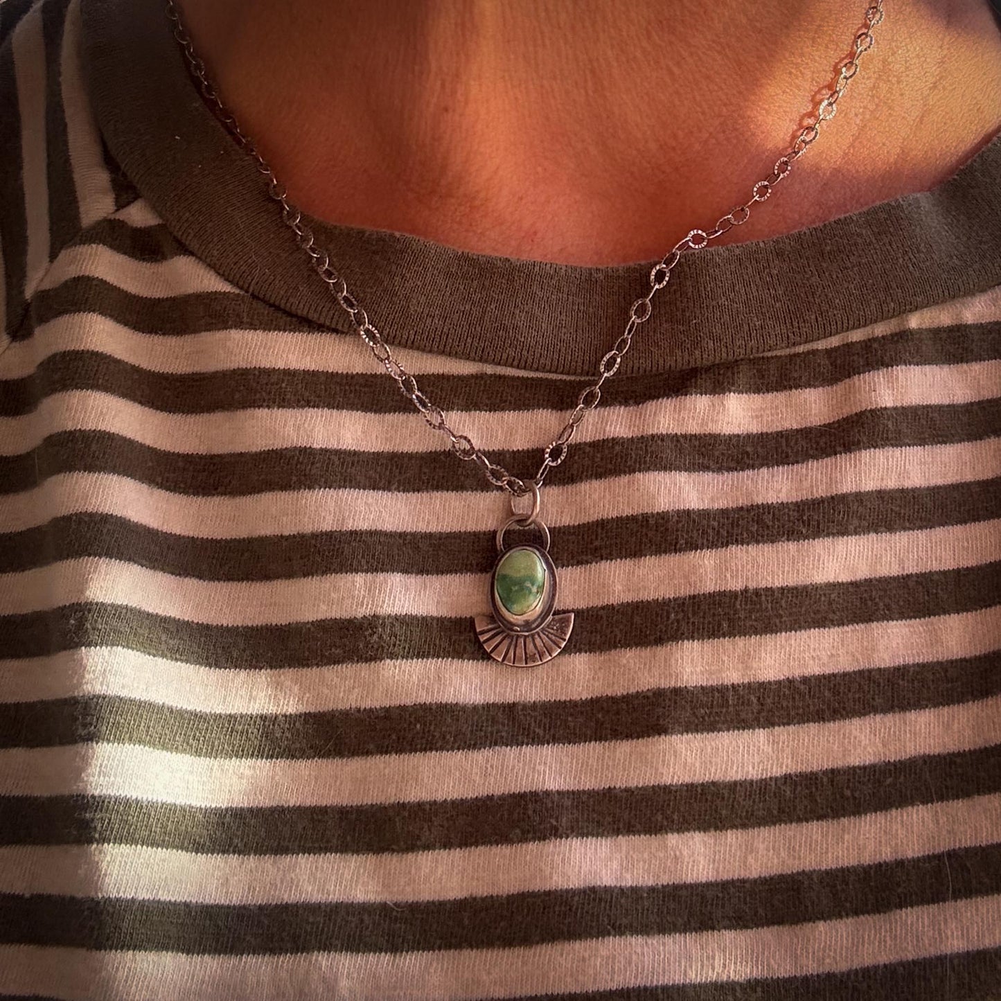 Necklace with a green pendant worn by a person in a striped shirt