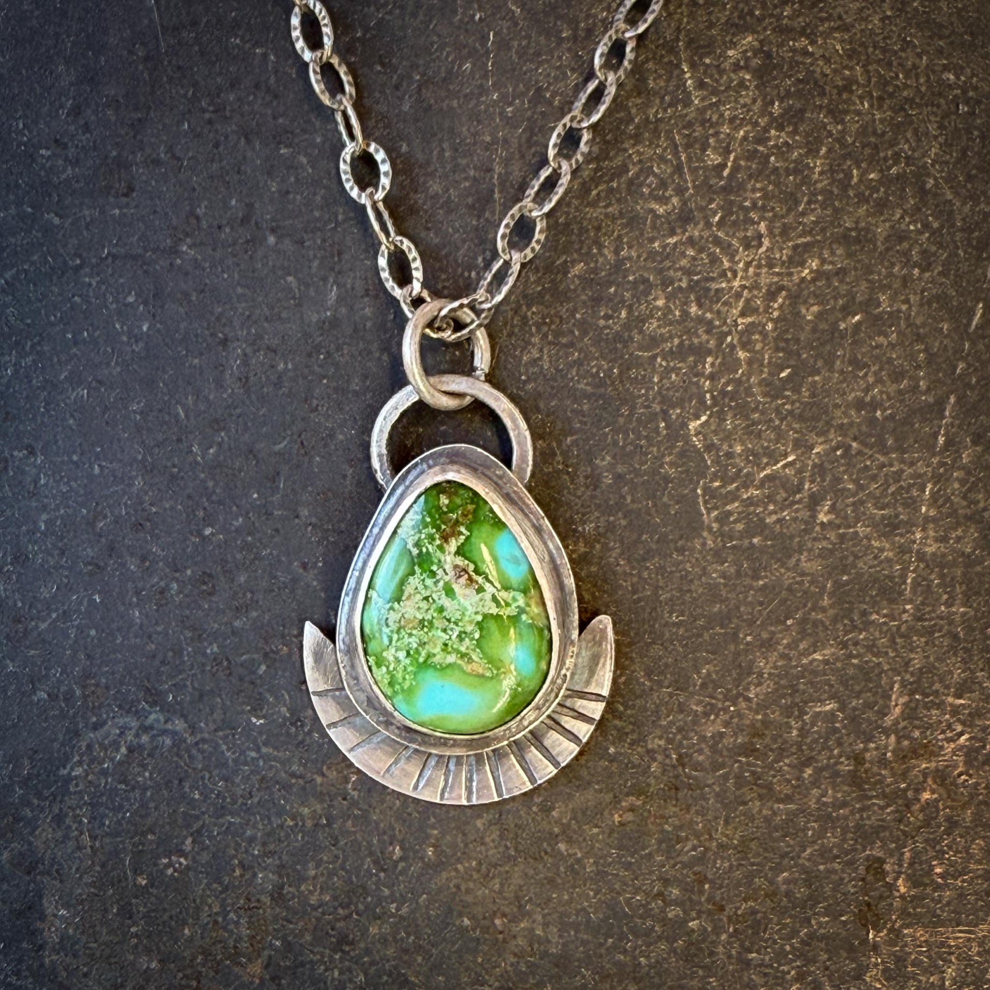 Necklace with a green teardrop pendant on a textured dark background