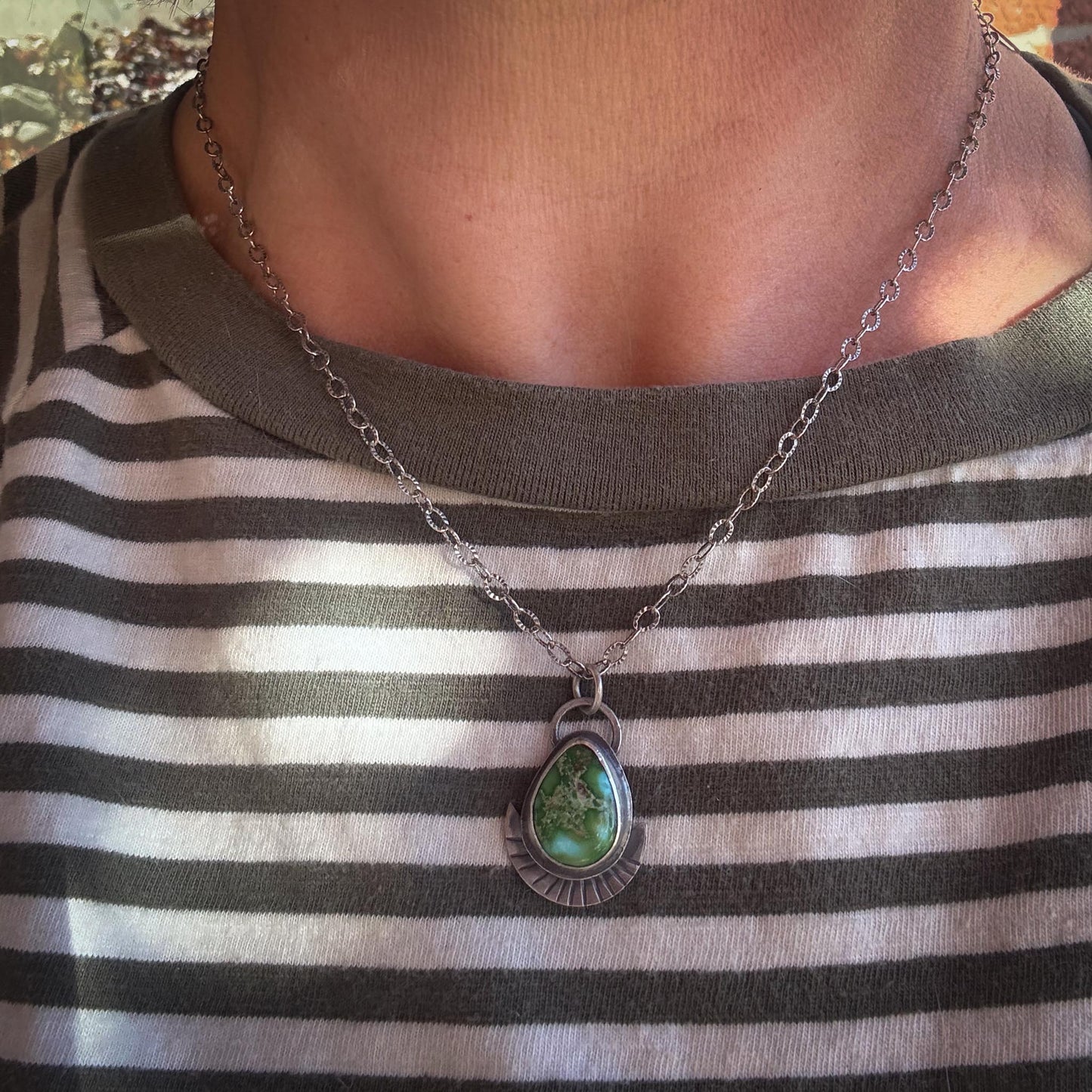 Necklace with a green pendant worn by a person in a striped shirt