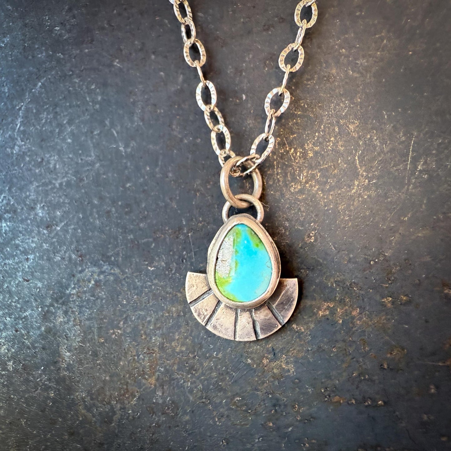 Necklace with a pendant featuring a turquoise stone on a textured dark surface
